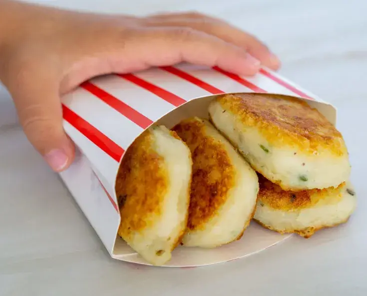 Caucasian hand on a red-and-white-striped food pail holding 4 mashed potato nuggets with chives