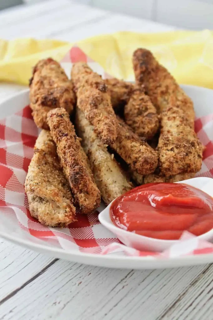 Chicken tenders on a red-and-white checkered liner, with a small bowl of ketchup