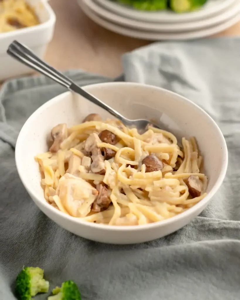 Chicken tetrazzini in a white bowl, with a silver eating utensil, atop a grey towel