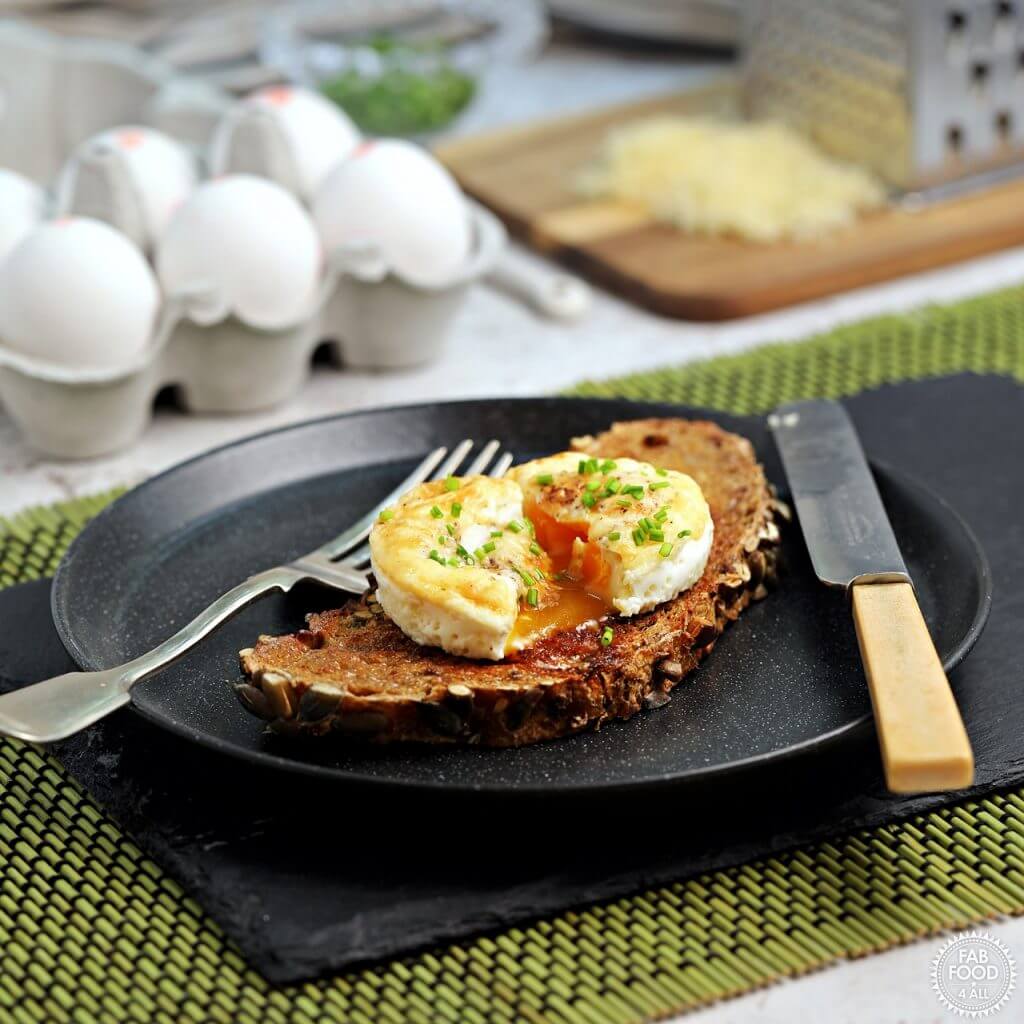 Slightly runny yolk baked egg on a brown piece of bread, sitting on a black plate